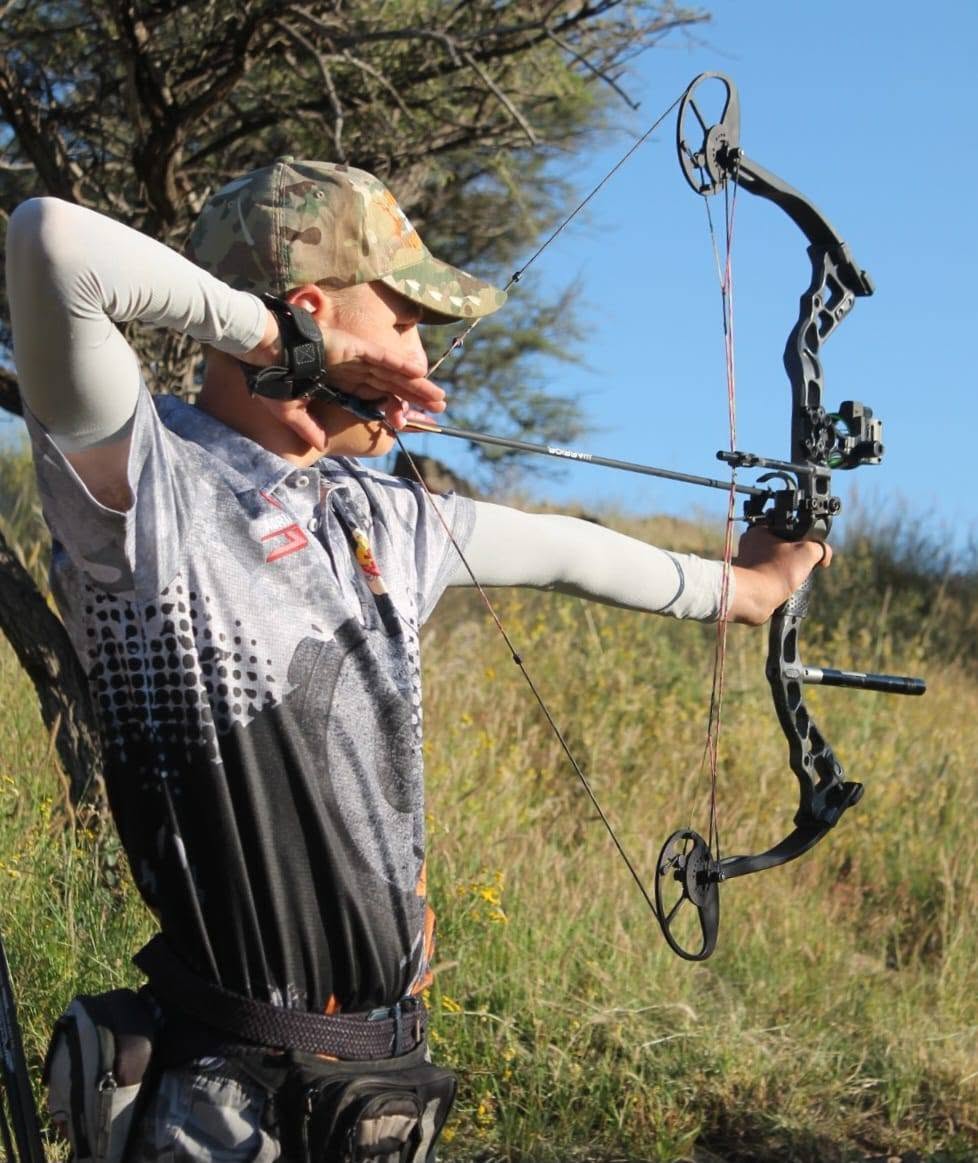 Archer drawing a compound bow among golden grass and acacia at Yellowstone